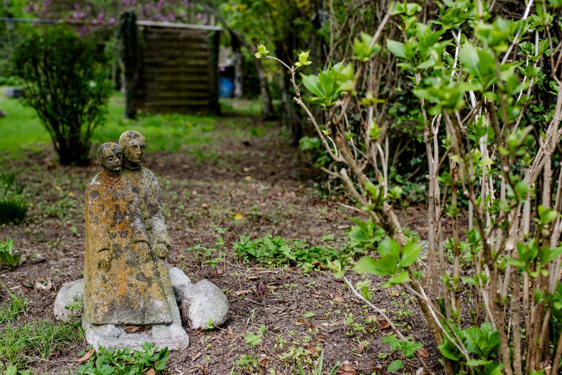 Detailaufnahme einer moosbewachsenen Gartenskulptur in einem naturbelassenen Gartenbereich.