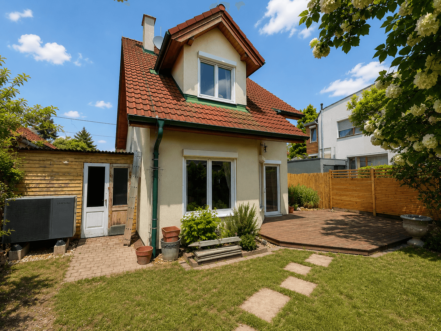Hinteransicht des Einfamilienhauses mit gepflegtem Garten, Holzterrasse und einem kleinen Schuppen.