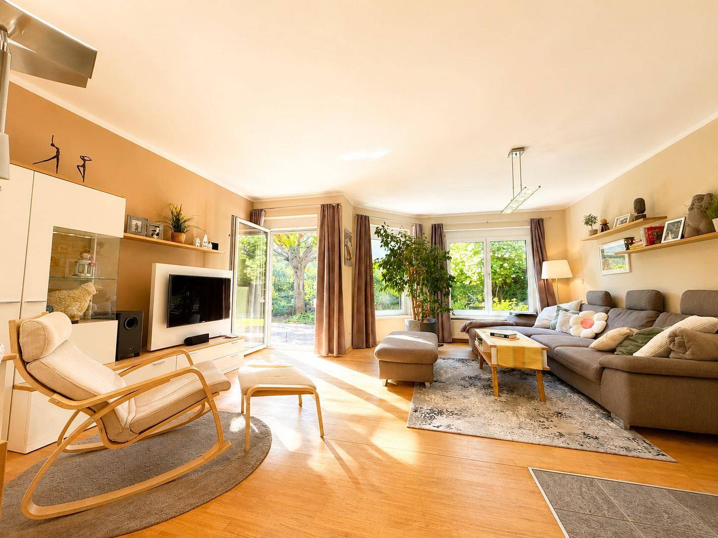 Helles Wohnzimmer mit Holzboden, bequemer Couch und Zugang zur Terrasse mit Blick in den Garten.