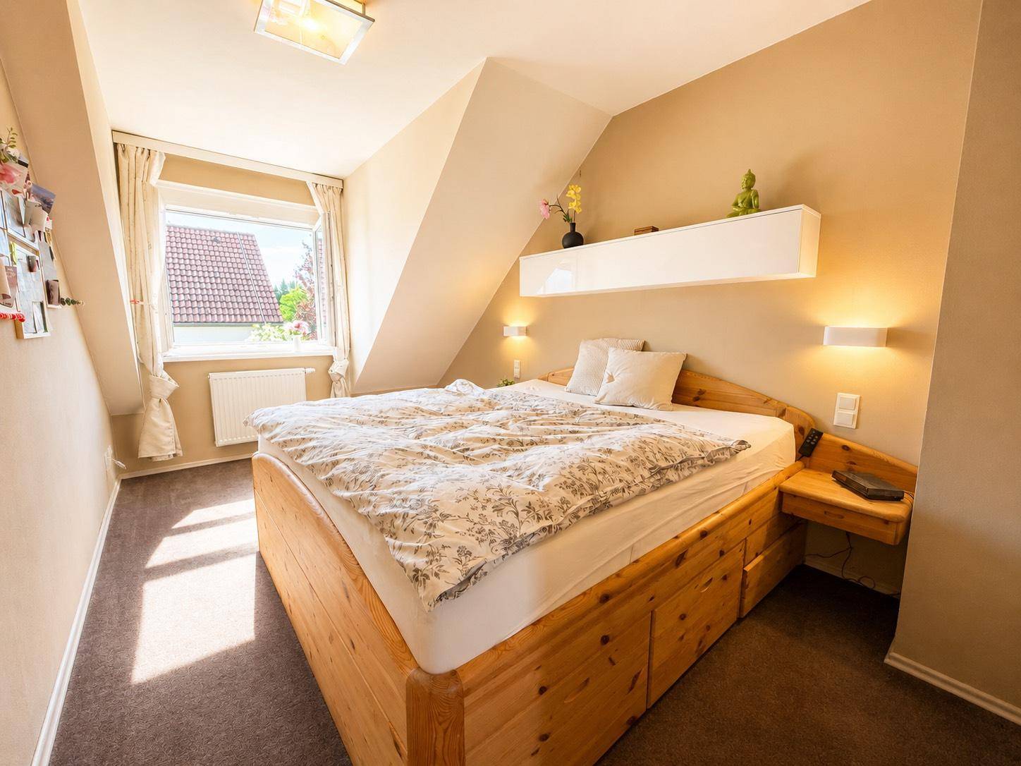 Gemütliches Schlafzimmer im Dachgeschoss mit Holzbett, Teppichboden und schrägen Wänden.