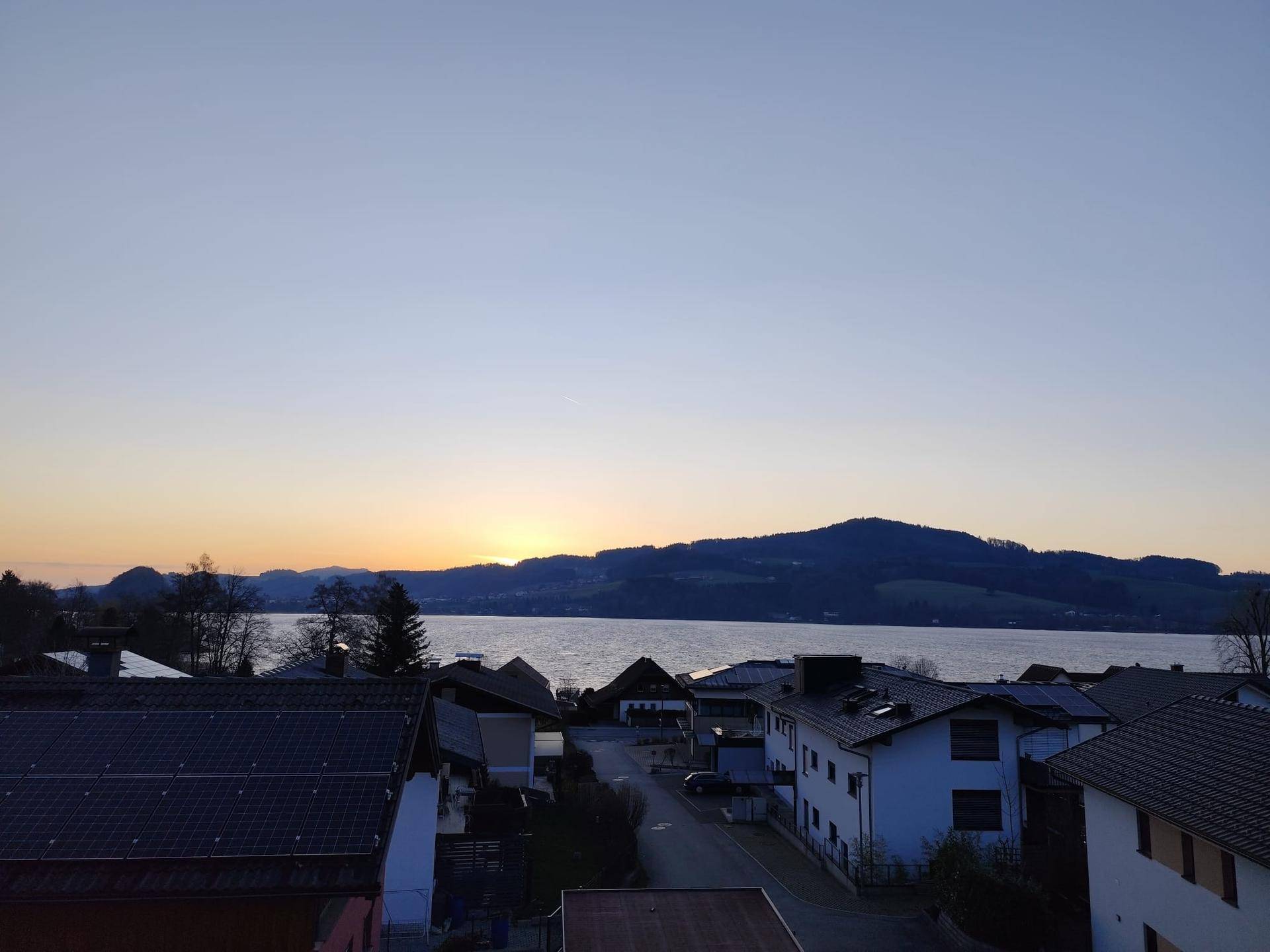 Malerischer Sonnenuntergang über dem See mit sanften Hügeln im Hintergrund.