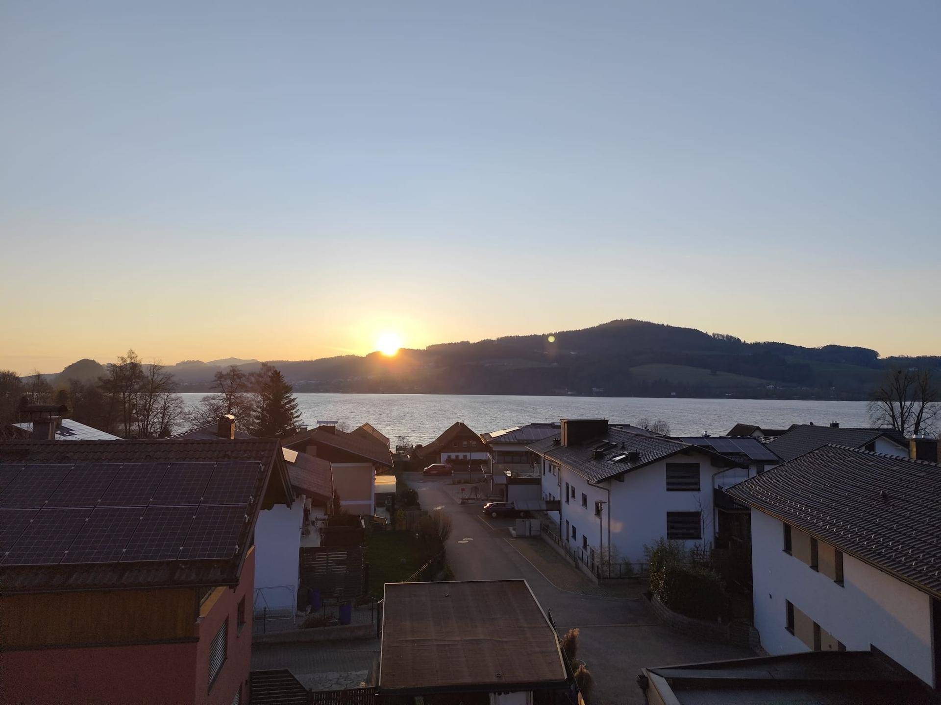 Strahlender Sonnenaufgang über dem See, der die Landschaft in warmes Licht taucht.