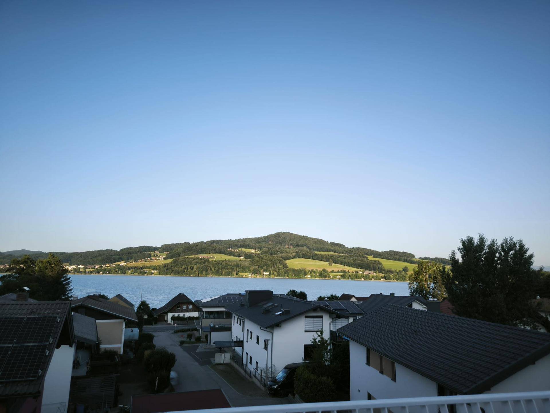Panoramablick auf den See und die grüne Umgebung unter einem weiten blauen Himmel.