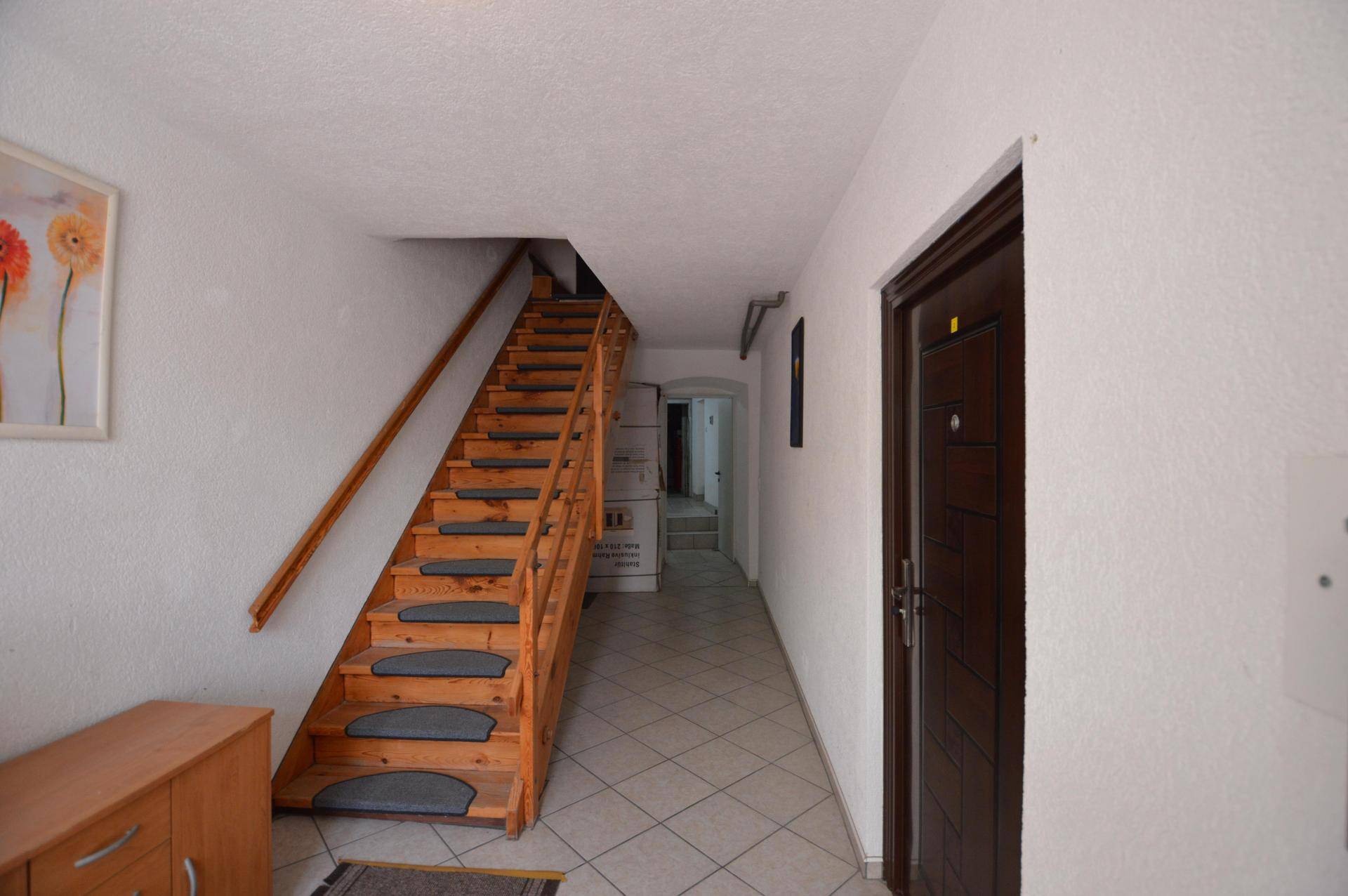 Heller Flur mit Holztreppe und weiß gefliestem Boden, der zu weiteren Räumen führt.