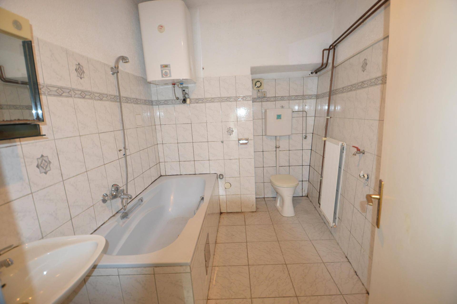 Gefliestes Badezimmer mit Badewanne, Waschbecken und Toilette, ausgestattet mit einem Warmwasserboiler.