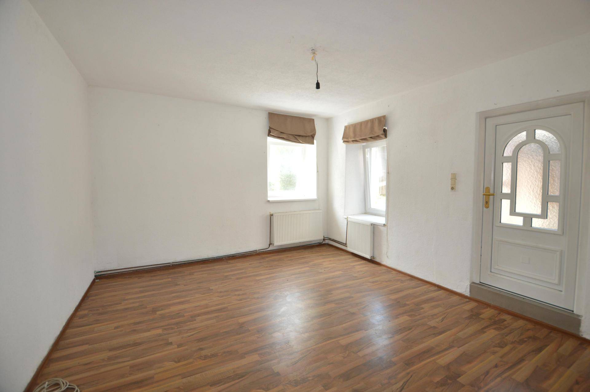 Heller Raum mit Laminatboden und zwei Fenstern, bereit zur individuellen Gestaltung.