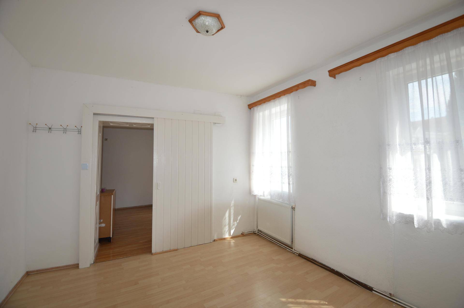 Helles Schlafzimmer mit Laminatboden und zwei Fenstern, durch eine Schiebetür zugänglich.