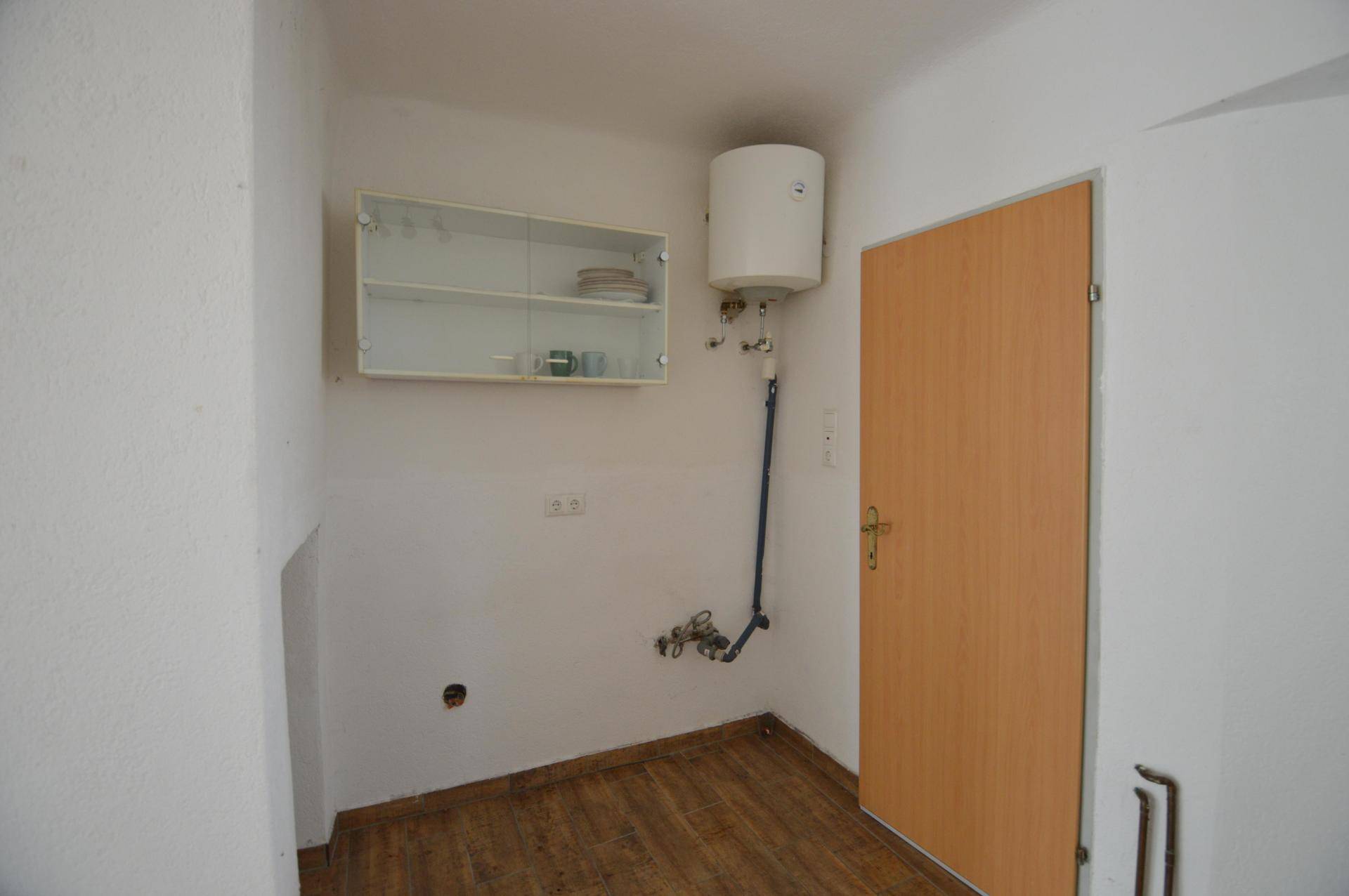 Kleiner Raum mit Warmwasserboiler und einem Hängeschrank, ideal als Abstell- oder Hauswirtschaftsraum.