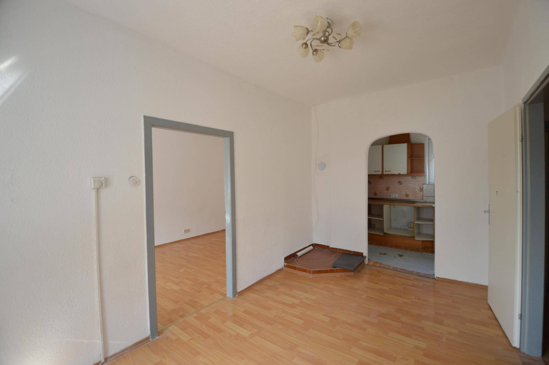 Wohnraum mit Laminatboden und einem Durchgang zu einer kleinen Küchennische.