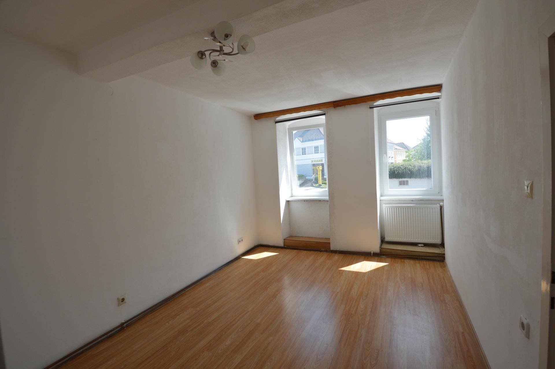 Heller Wohnraum mit Laminatboden und zwei Fenstern, die viel Tageslicht hereinlassen.