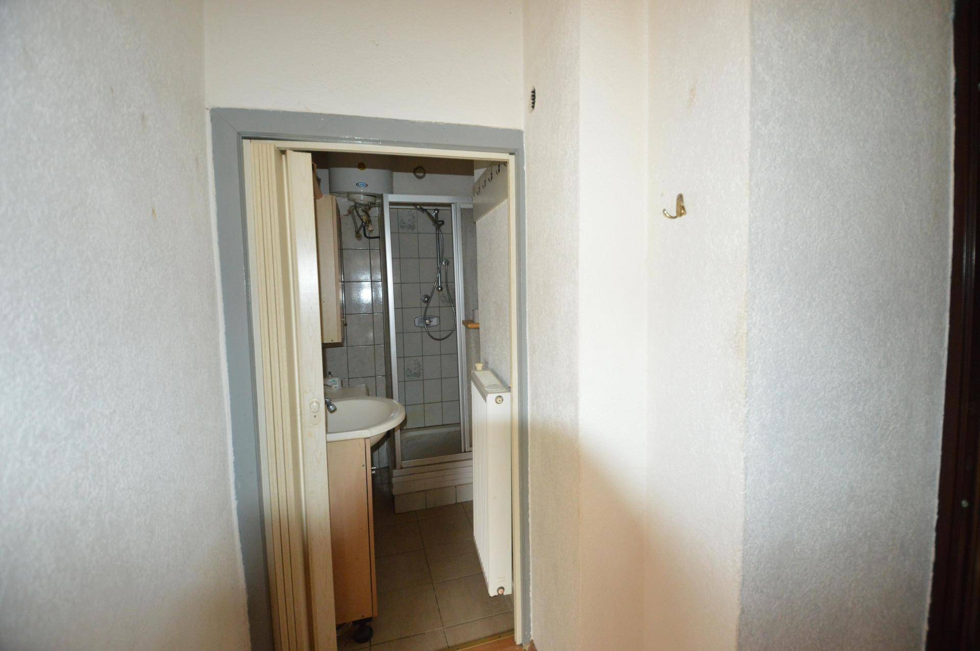 Eingangsbereich zu einem Badezimmer mit Duschkabine und Waschbecken, funktional eingerichtet.