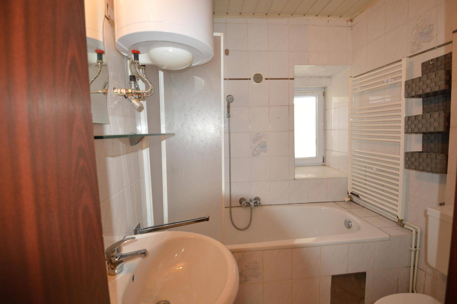 Gefliestes Badezimmer mit Badewanne, Waschbecken und beheiztem Handtuchhalter, hell durch ein Fenster.
