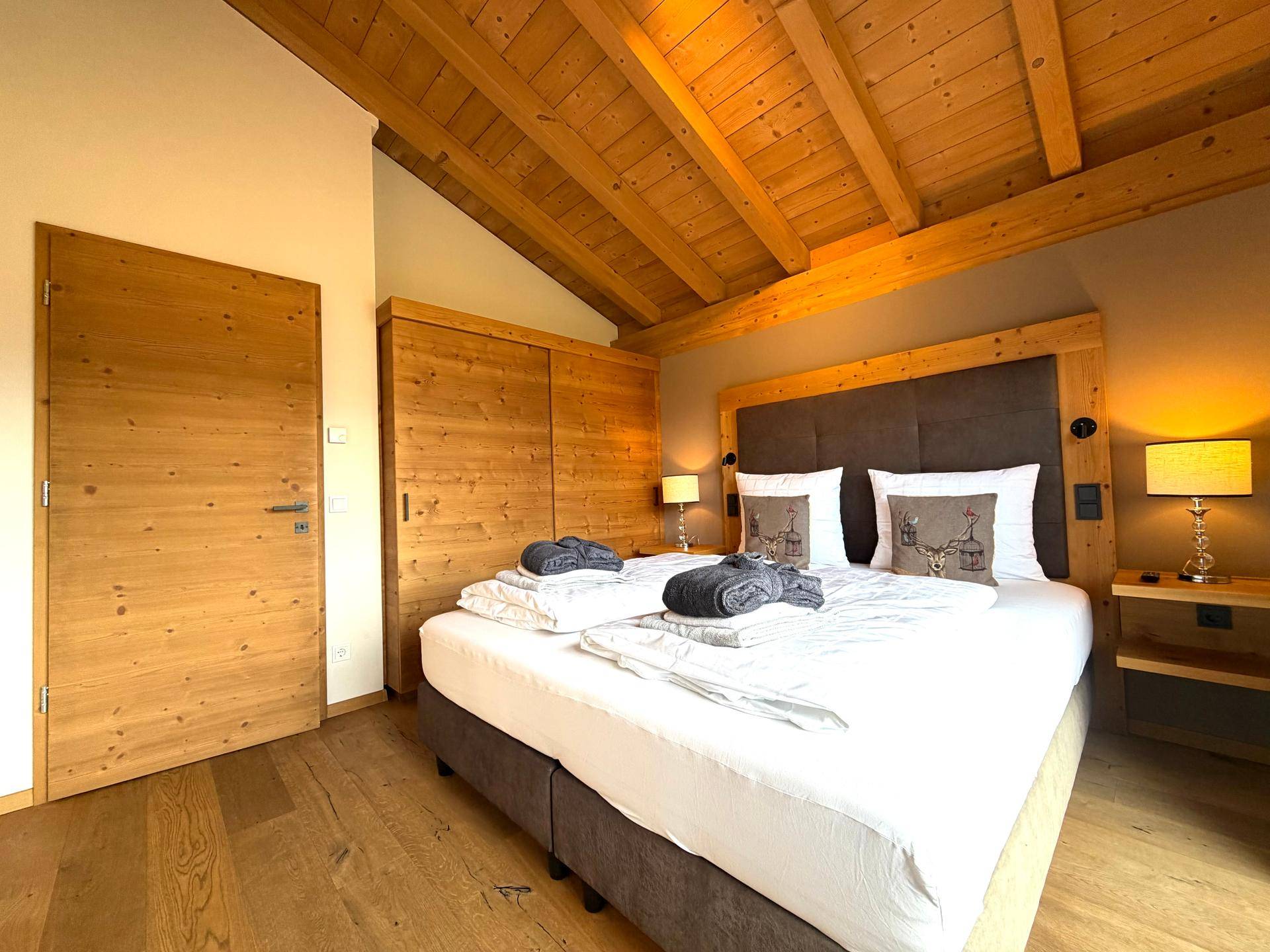 Komfortables Schlafzimmer mit Holzbalkendecke, Doppelbett und Holztür in modernem Stil.
