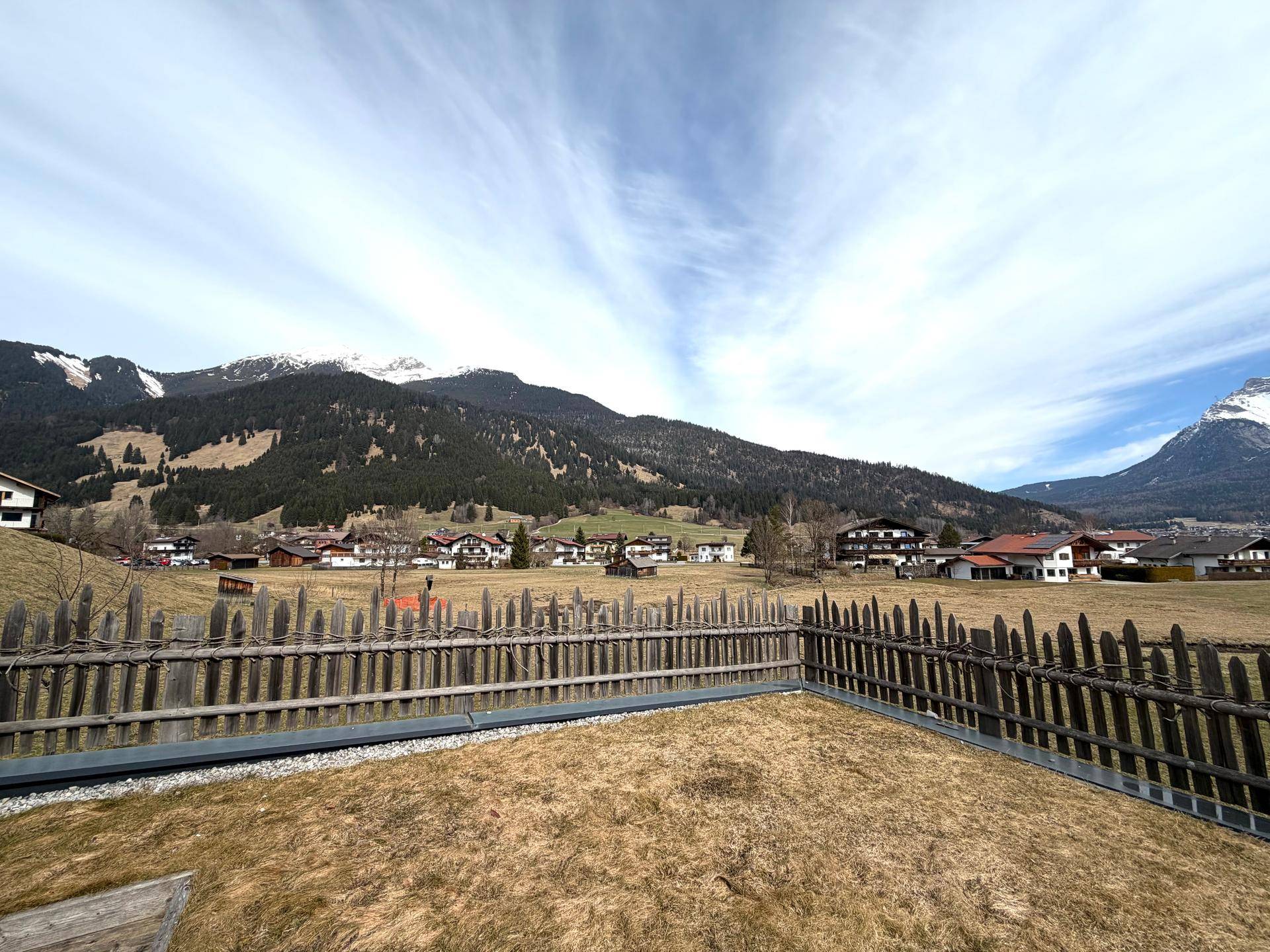 Panoramablick auf die alpine Landschaft mit Bergen und weiten Feldern unter klarem Himmel.