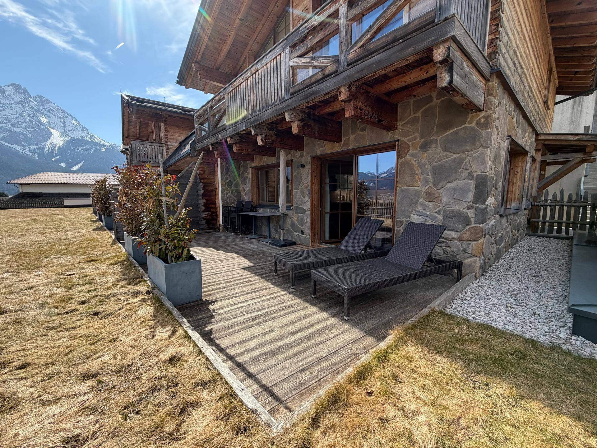 Sonnenterrasse mit Holzdeck, Liegestühlen und Blick auf die umliegende Berglandschaft.