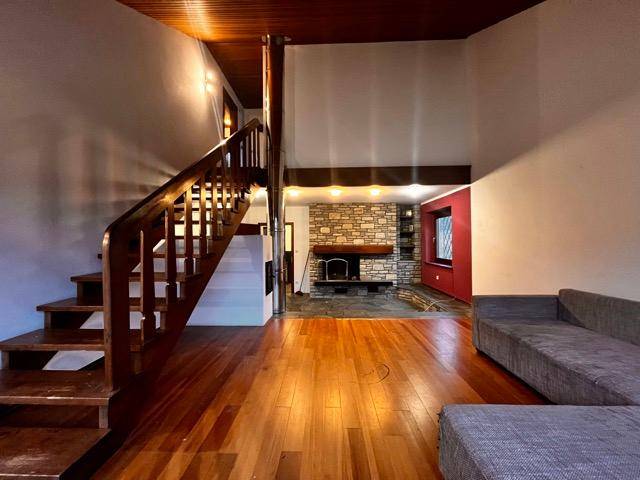 Geräumiges Wohnzimmer mit Holztreppe, Parkettboden und einem markanten Steinkamin.