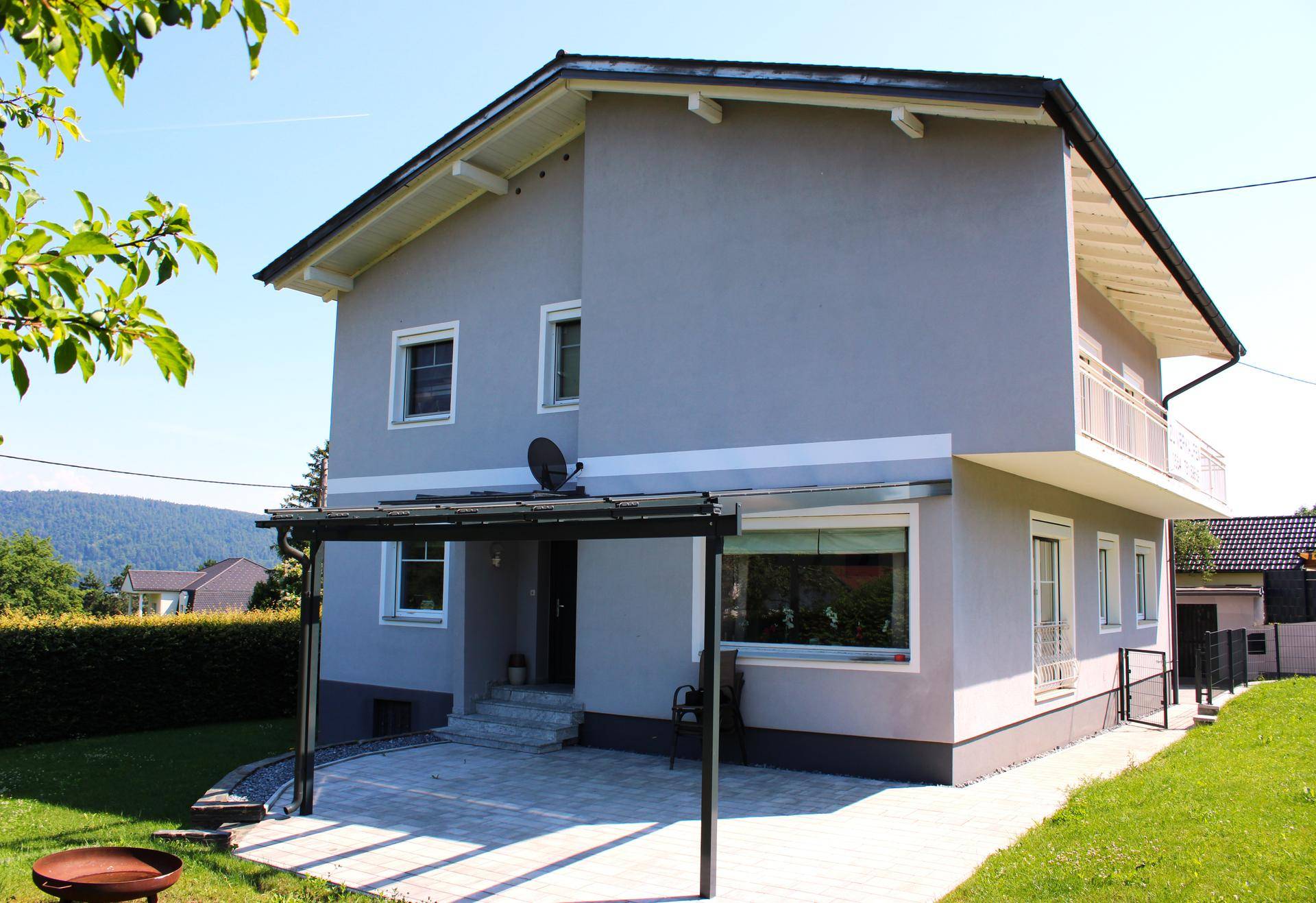 Graues Einfamilienhaus mit überdachter Terrasse und gepflegtem Gartenbereich.