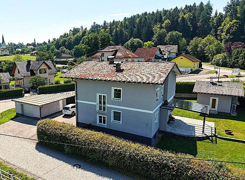 Luftaufnahme eines Einfamilienhauses mit Garten, Garage und umliegender Landschaft.
