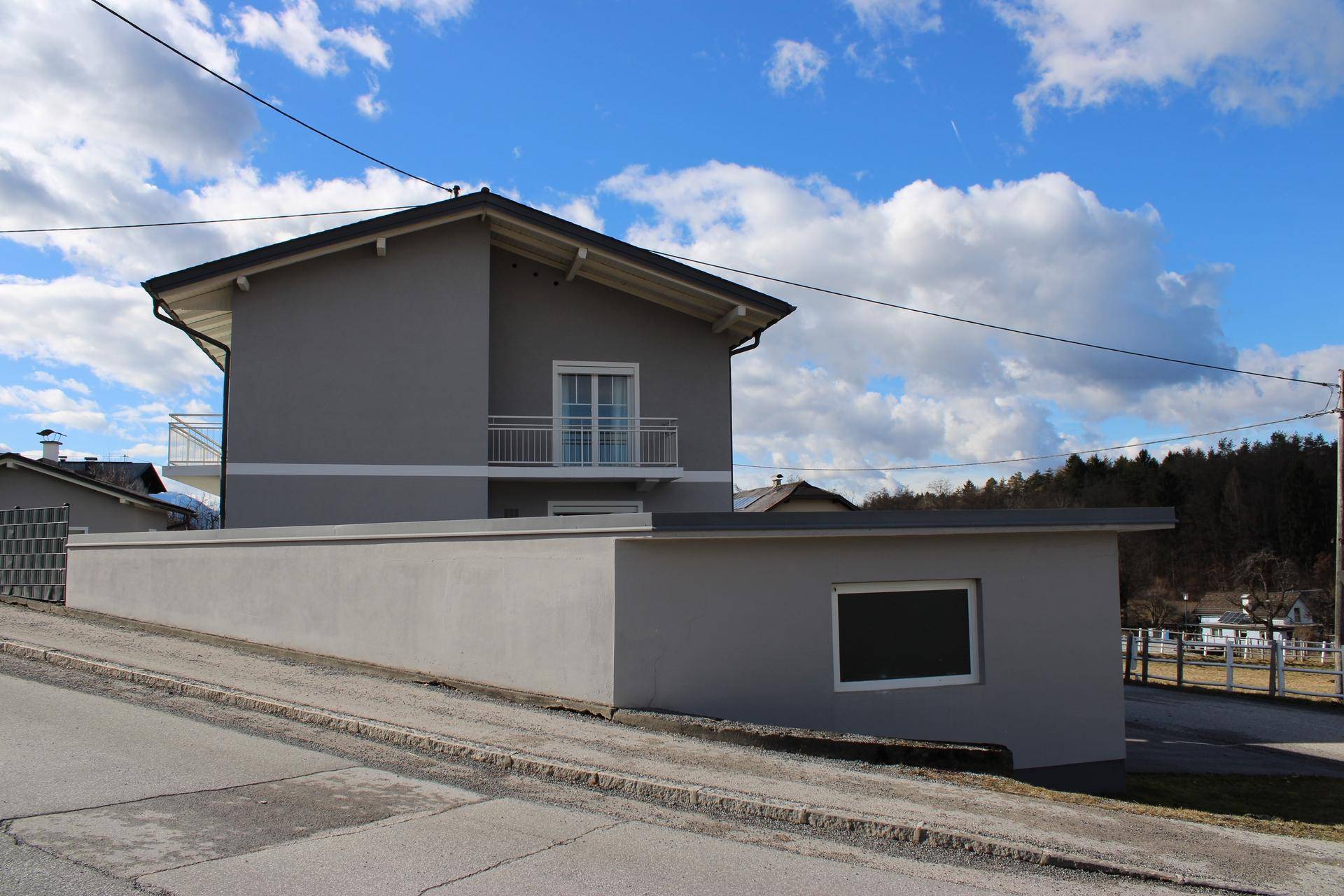 Graues Haus mit angrenzender Mauer und Garage, von der Straße aus gesehen.