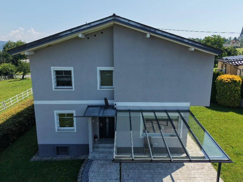 Vorderansicht eines modernen Einfamilienhauses mit überdachtem Eingangsbereich und Garten.