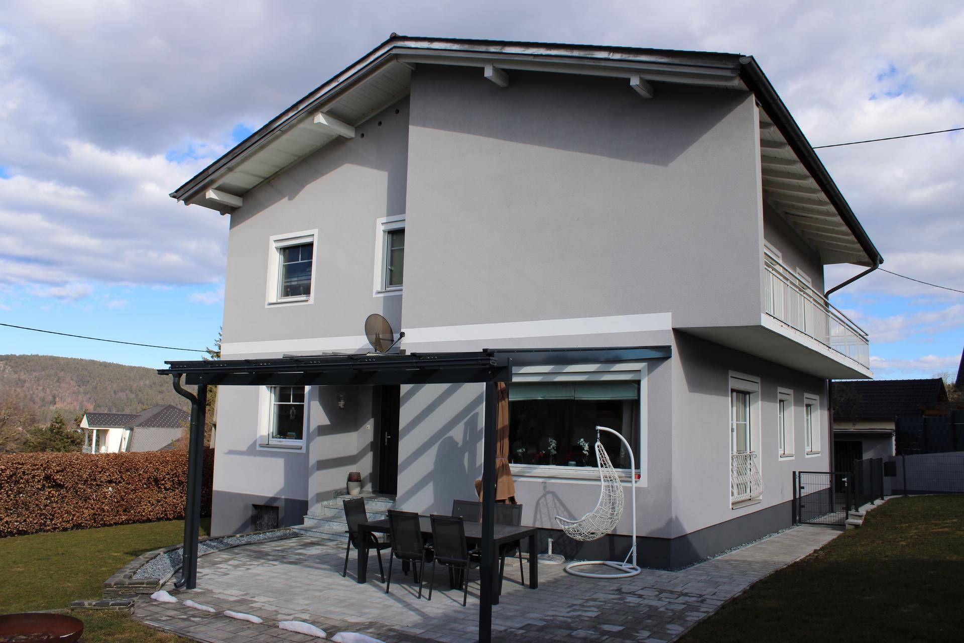 Modernes Einfamilienhaus mit möblierter, überdachter Terrasse und Gartenbereich.