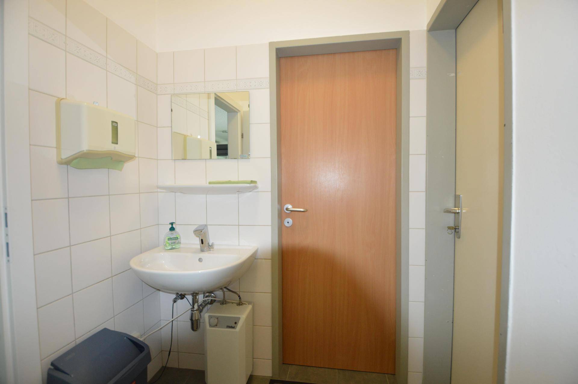 Funktionale Toilette mit Waschbecken, Spiegel und weißen Wandfliesen.
