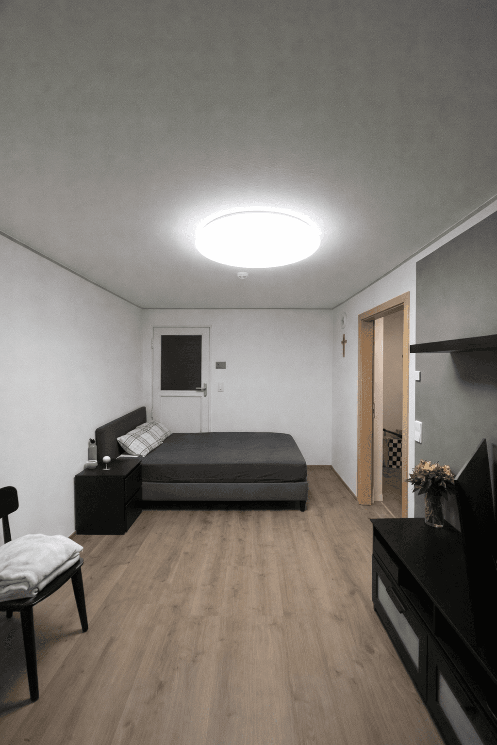 Gemütliches Schlafzimmer mit Bett, Nachttisch und Wandfernseher.