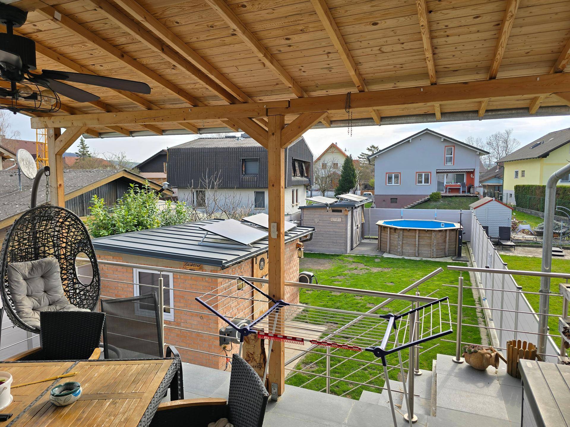 Überdachte Terrasse mit Holzdecke, Gartenmöbeln und Blick auf den Pool im Garten.