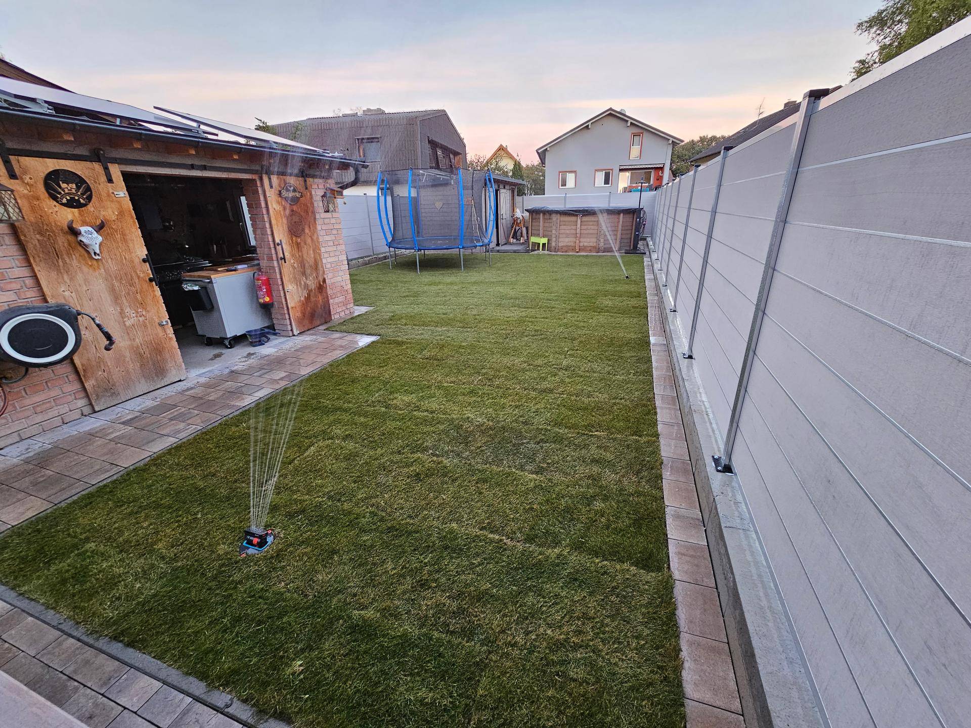 Gepflegter Garten mit Rasenfläche, Sprinklern und einem Trampolin.