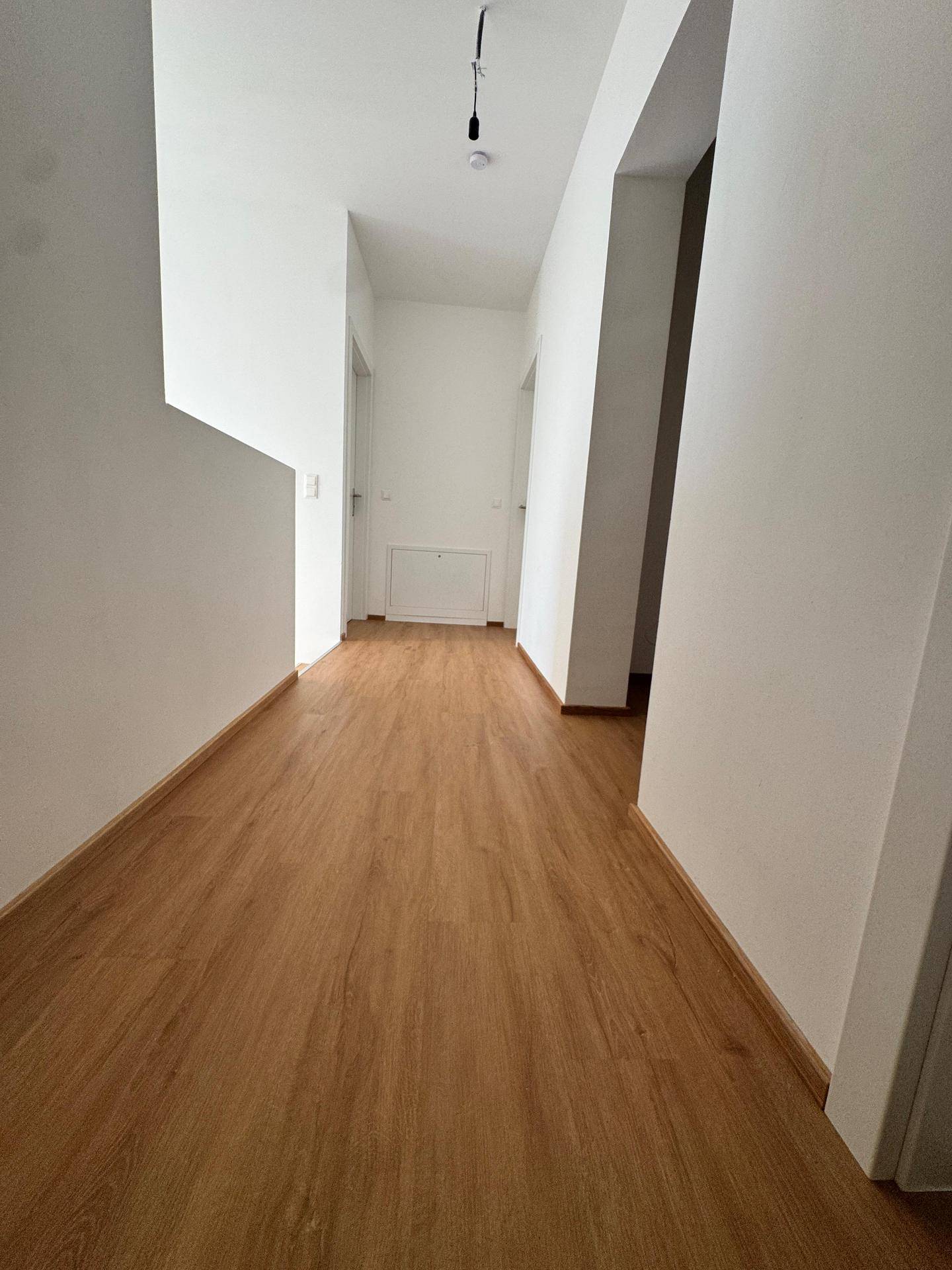 Langer, heller Flur mit Laminatboden und weißen Wänden, der verschiedene Räume verbindet.