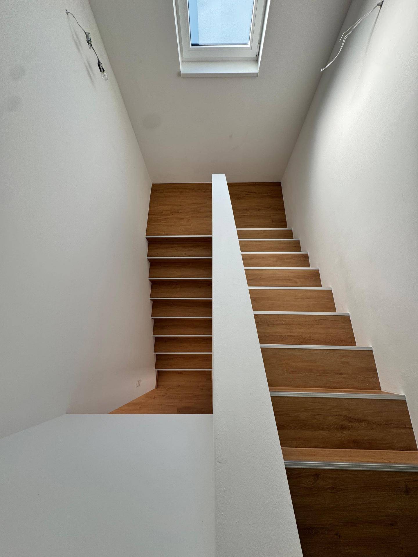 Heller Treppenaufgang mit Laminatstufen und einem Oberlicht, das natürliches Licht spendet.