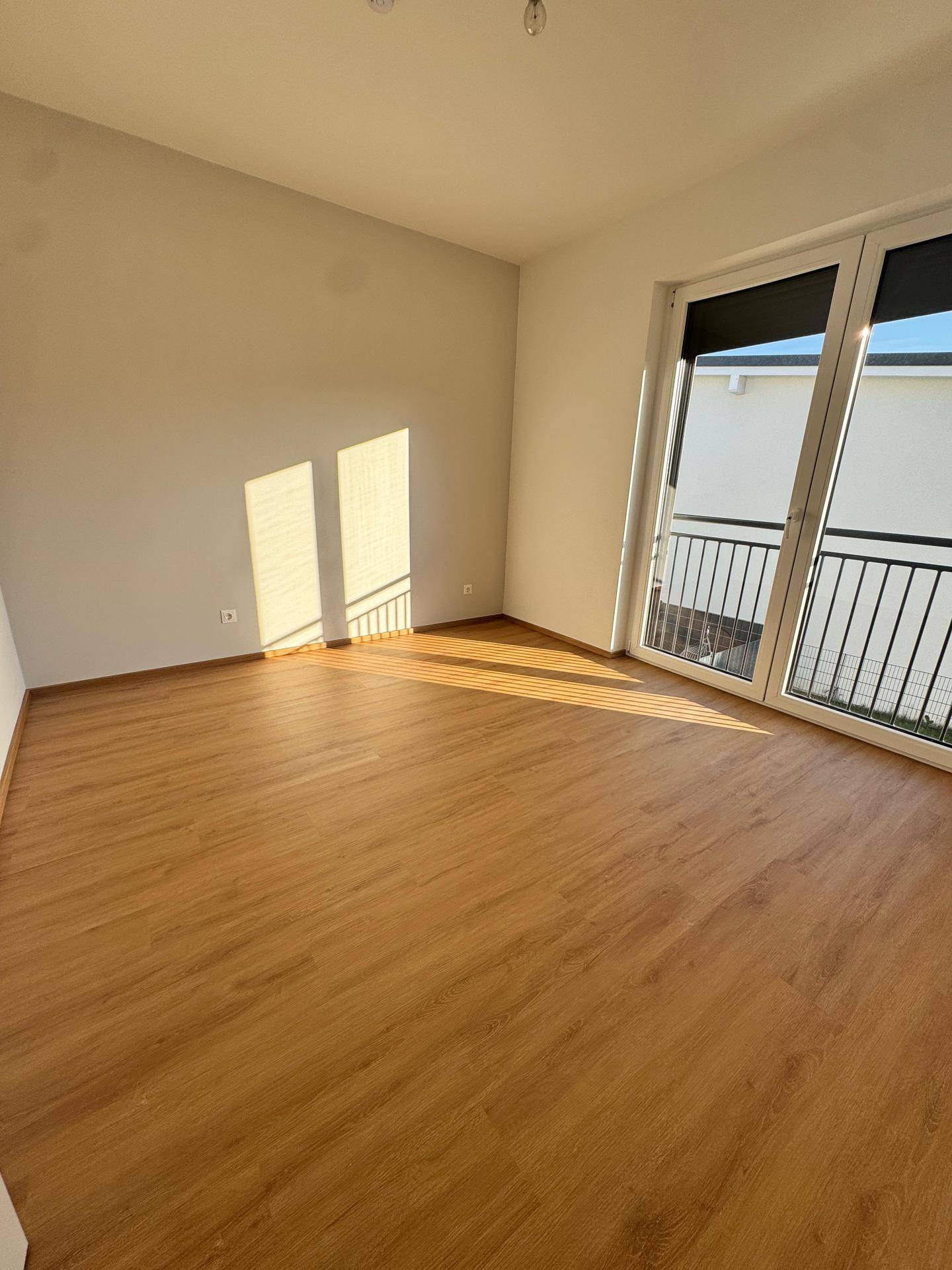 Helles Schlafzimmer mit Laminatboden und Zugang zu einem französischen Balkon, sonnendurchflutet.