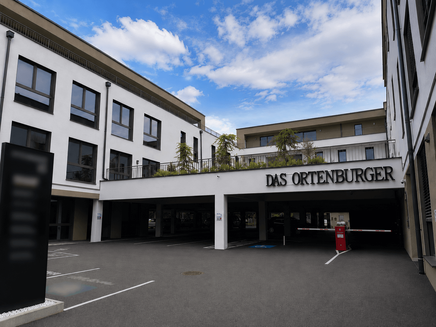 Eingangsbereich des Gebäudes "DAS ORTENBURGER" mit Zufahrt zur Tiefgarage und Parkplätzen.