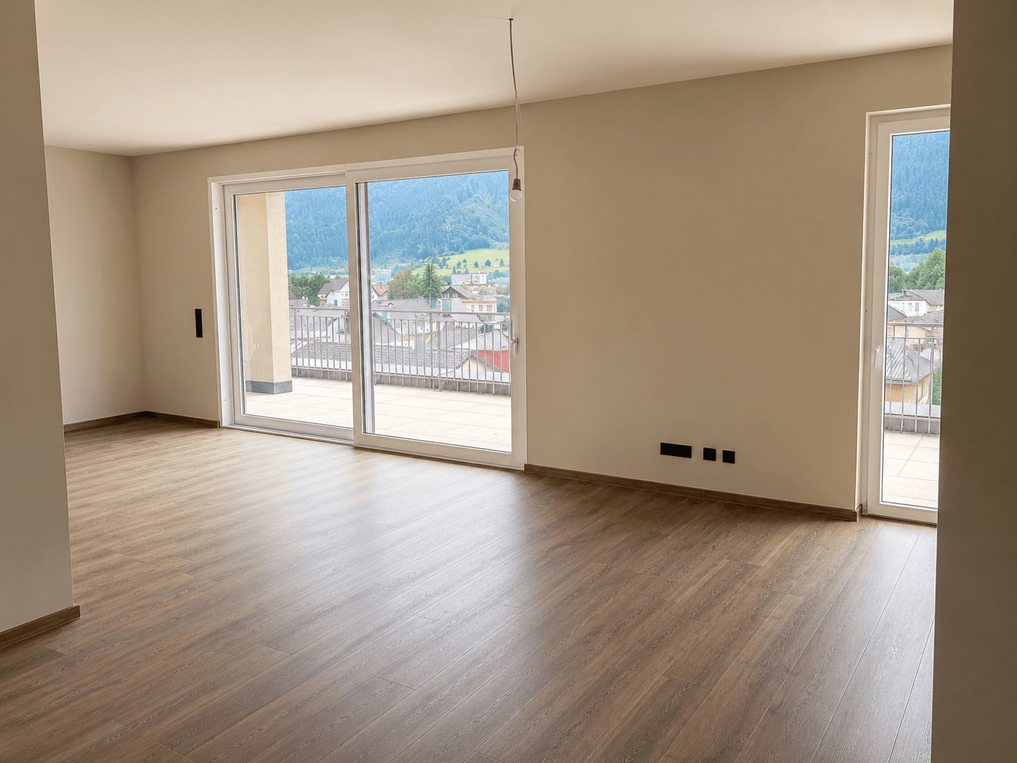 Geräumiger Wohnbereich mit Laminatboden und großen Schiebetüren zur Terrasse mit Bergblick.