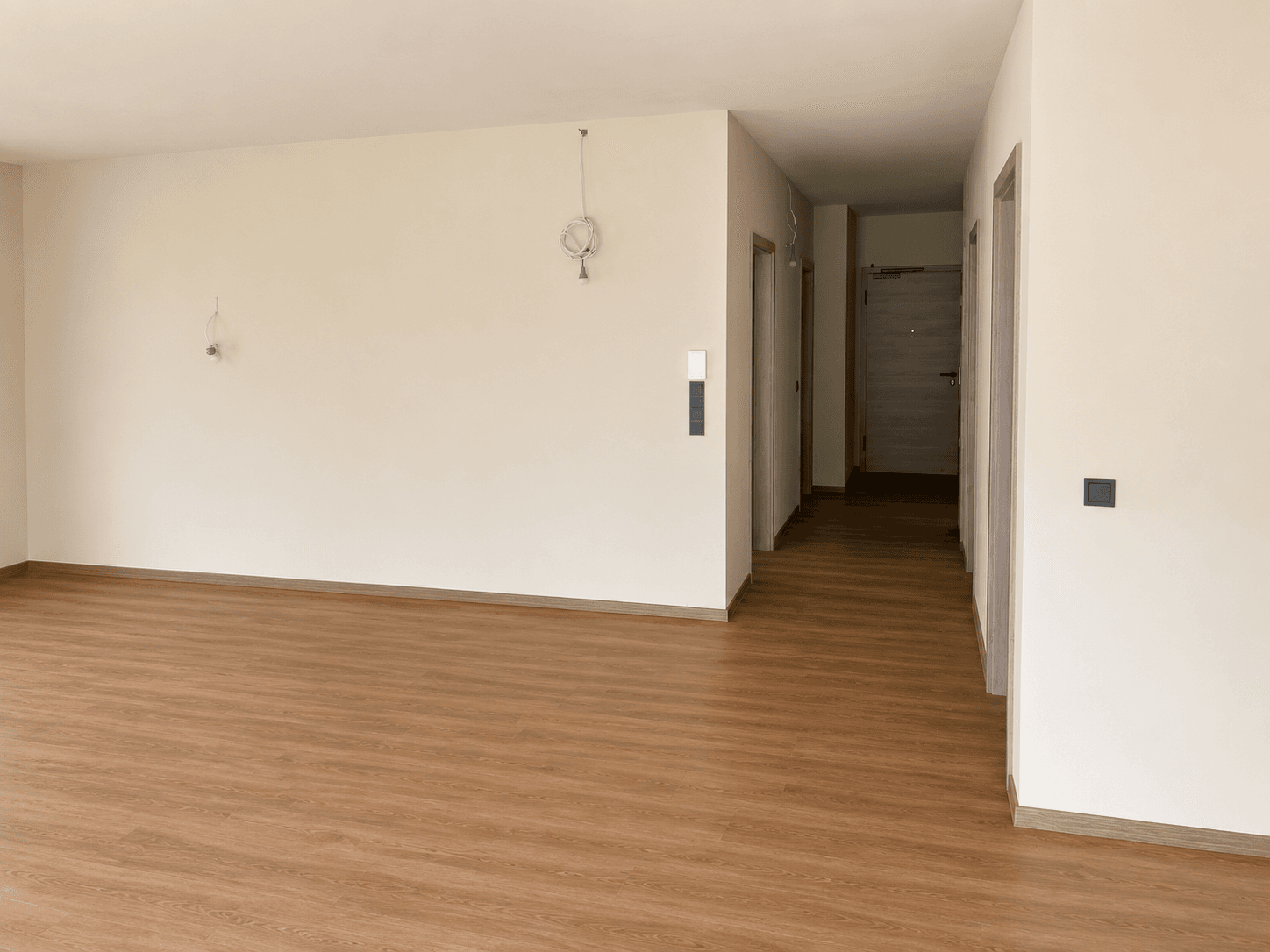 Geräumiger, unmöblierter Innenraum mit Laminatboden und Zugang zu einem Flur und weiteren Zimmern.