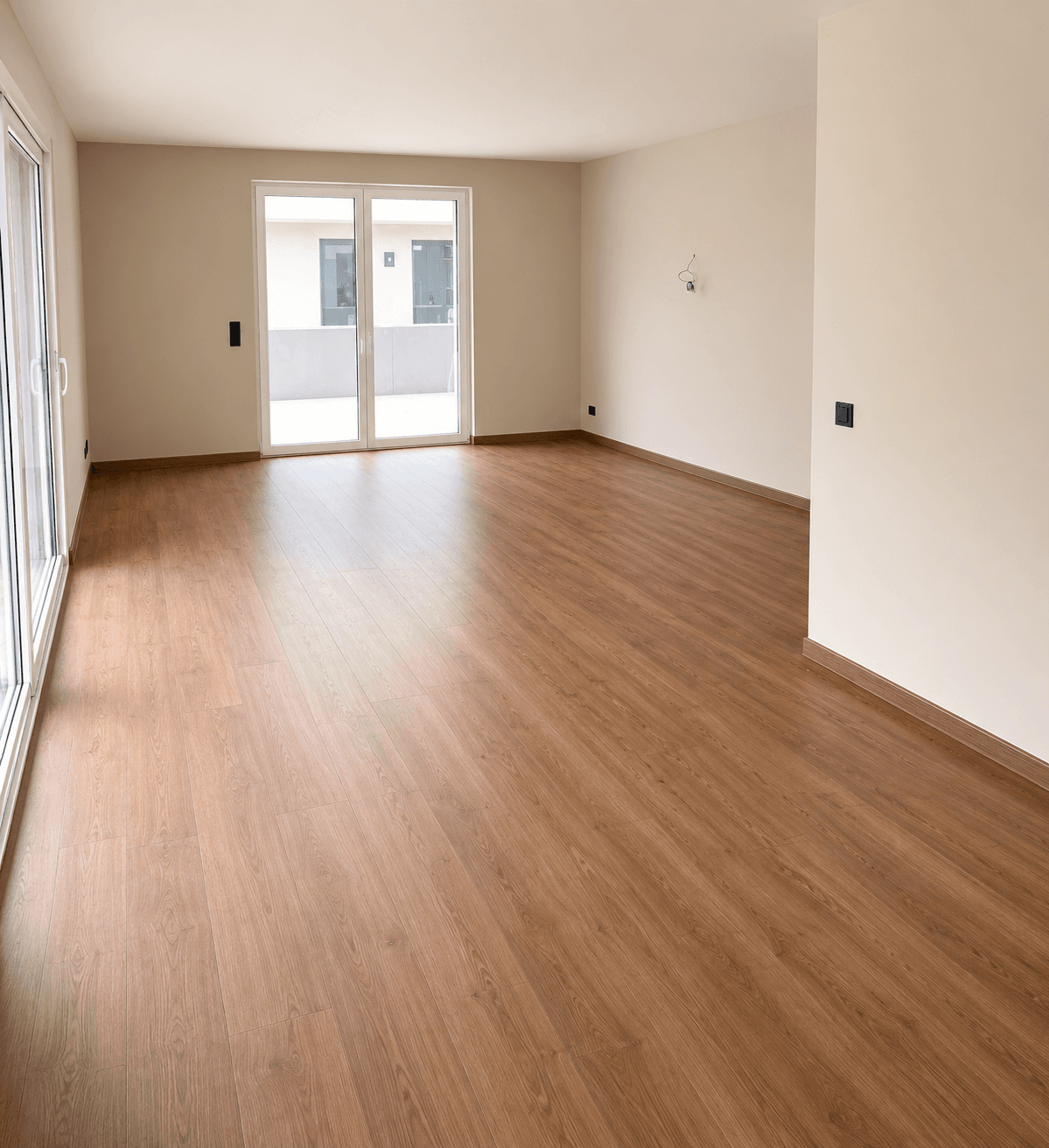 Lichtdurchfluteter, leerer Raum mit Laminatboden und zwei großen Fenstertüren, die nach draußen führen.