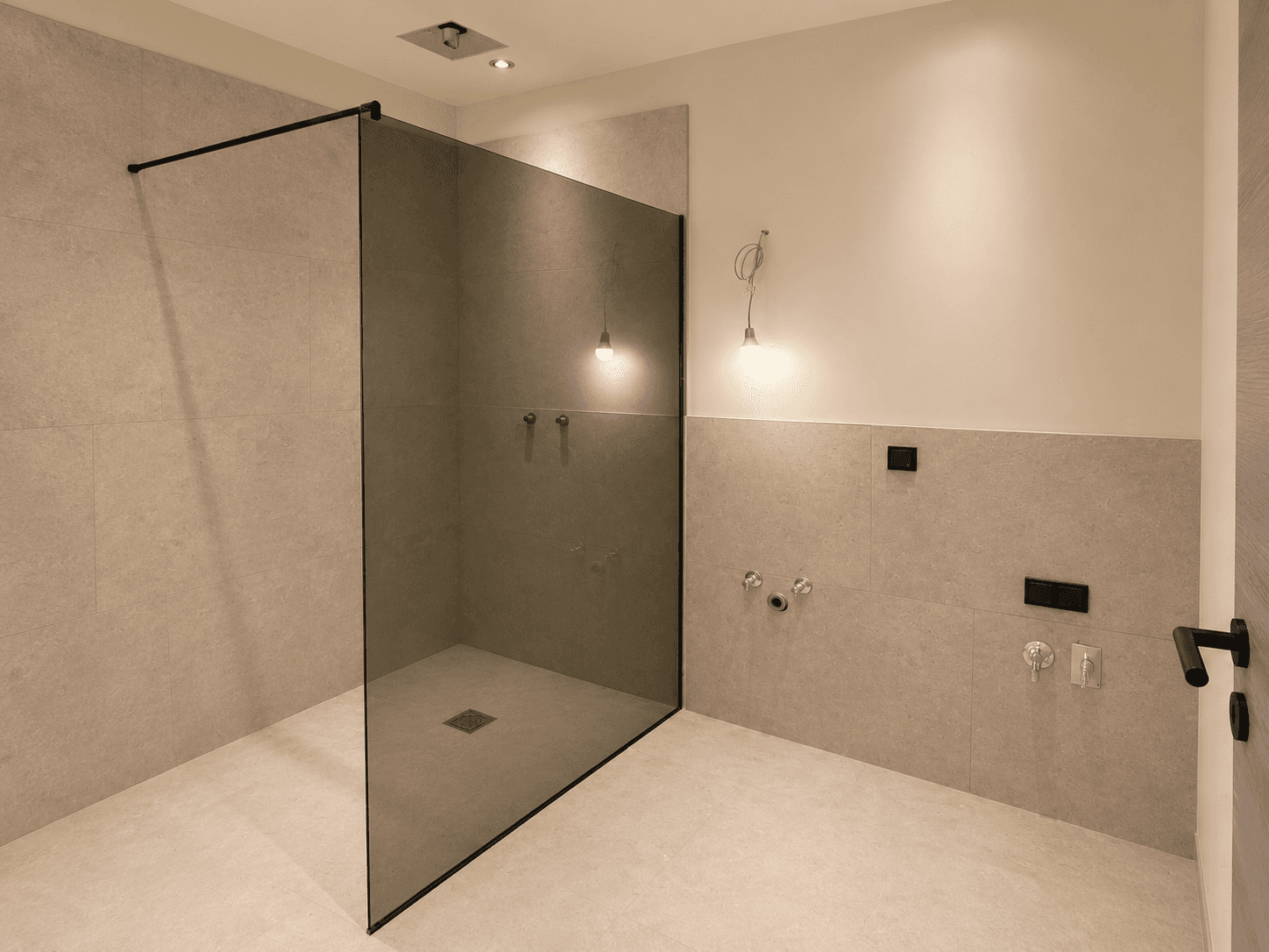 Modernes Badezimmer im Bau mit begehbarer Dusche, Glaswand und hellen Fliesen an Wänden und Boden.