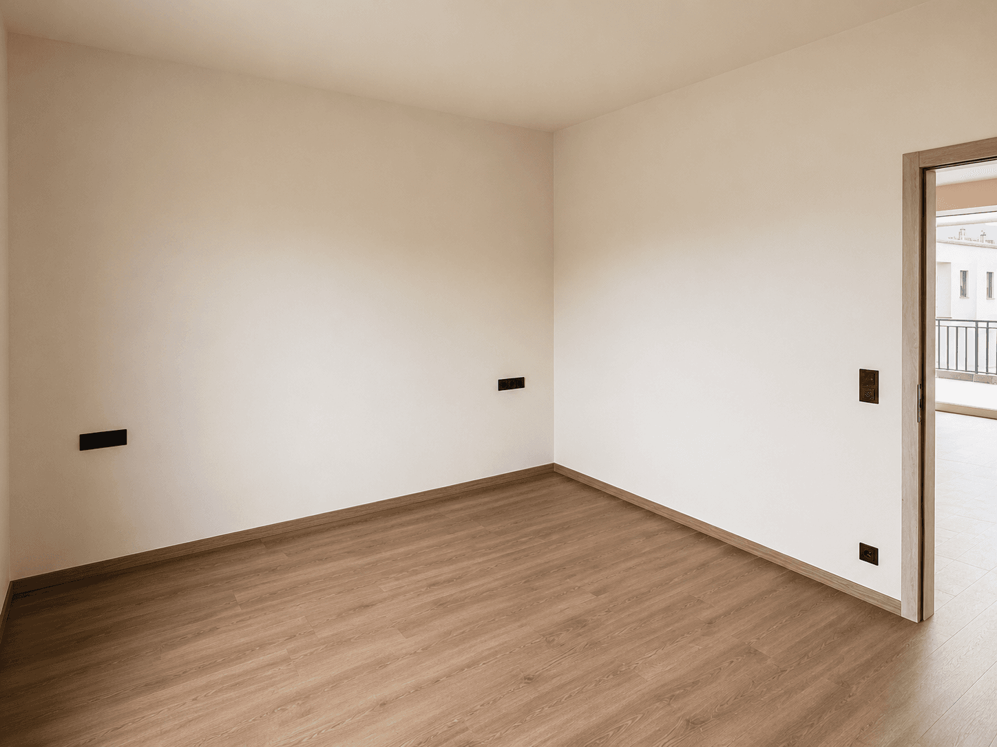 Leerer Raum mit Laminatboden und Zugang zu einem weiteren Zimmer mit Balkon.