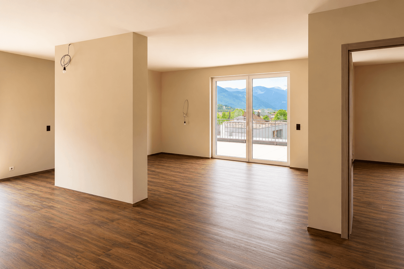 Heller, leerer Wohnraum mit Holzboden und Zugang zu einer großen Terrasse mit Bergblick.