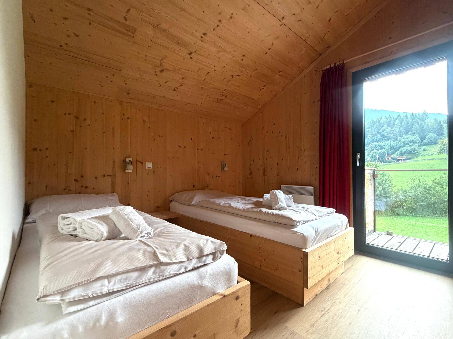 Helles Schlafzimmer mit zwei Einzelbetten, Holzwänden und Zugang zum Balkon.