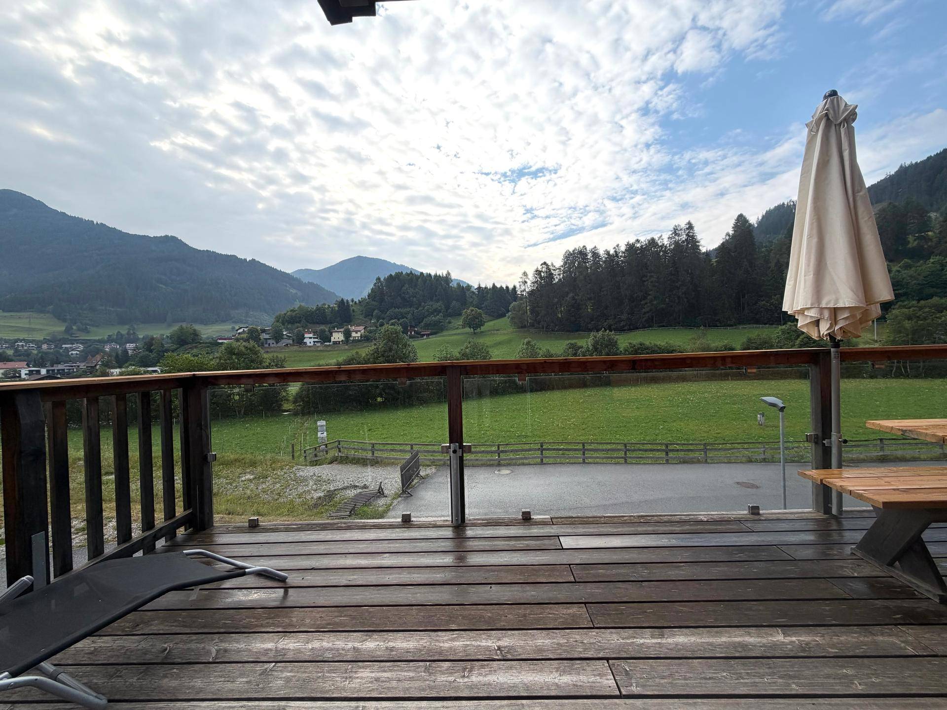 Großer Holzbalkon mit Liegestuhl und Sonnenschirm, ideal zum Entspannen mit Bergblick.