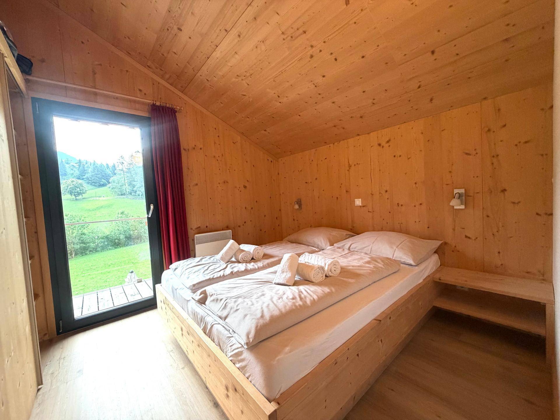 Gemütliches Schlafzimmer mit Doppelbett, Holzwänden und Blick auf die grüne Landschaft.