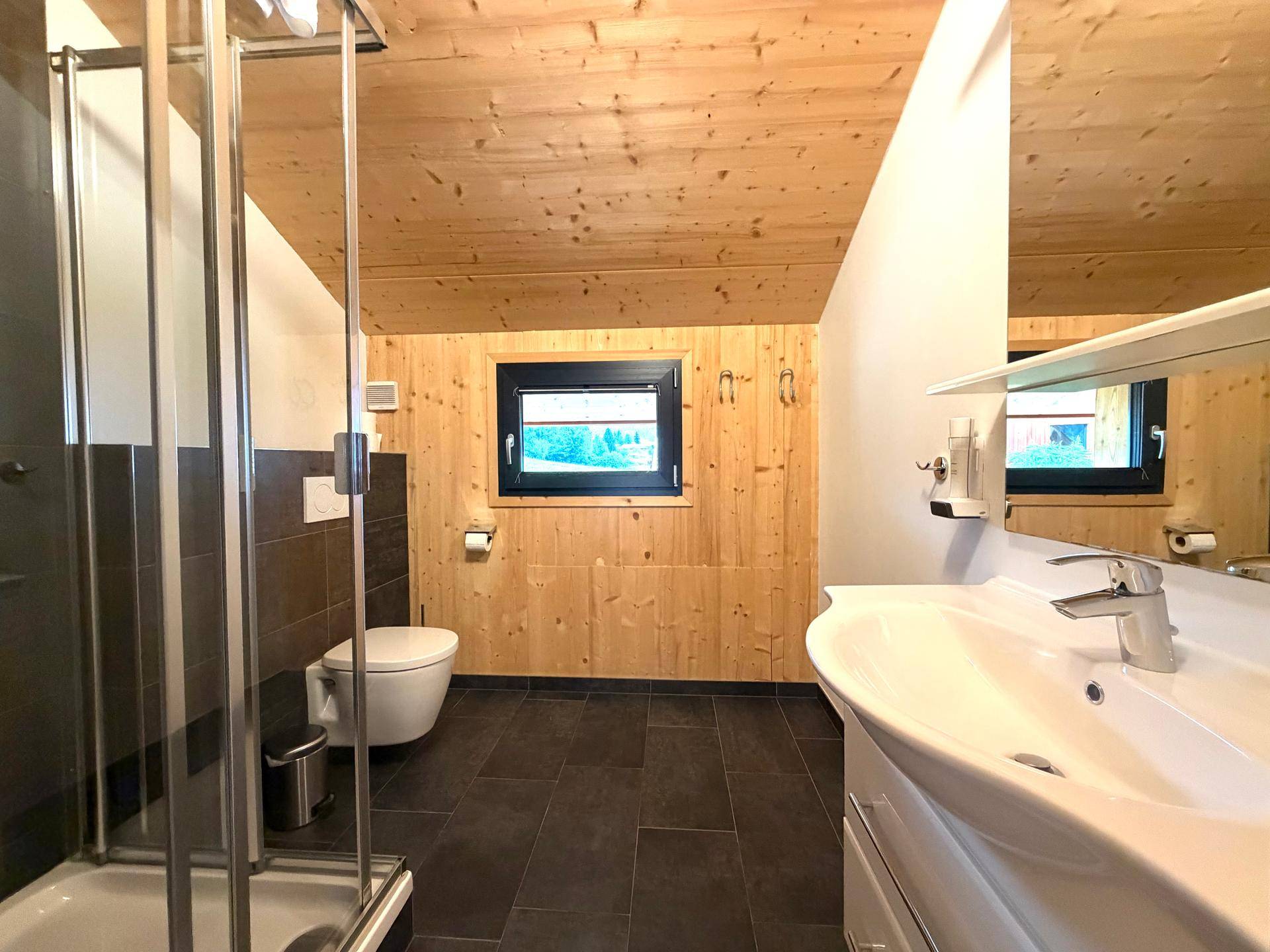 Modernes Badezimmer mit Dusche, WC, Waschbecken und Fenster.