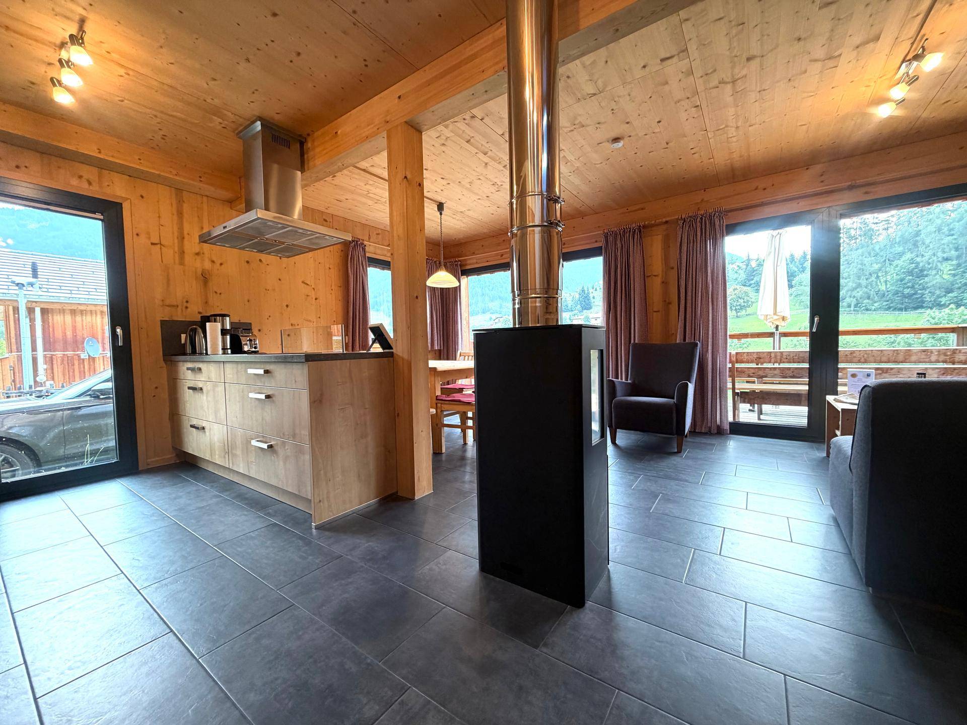 Offener Wohnbereich mit Kaminofen, Fliesenboden und großen Fenstern zur Terrasse.