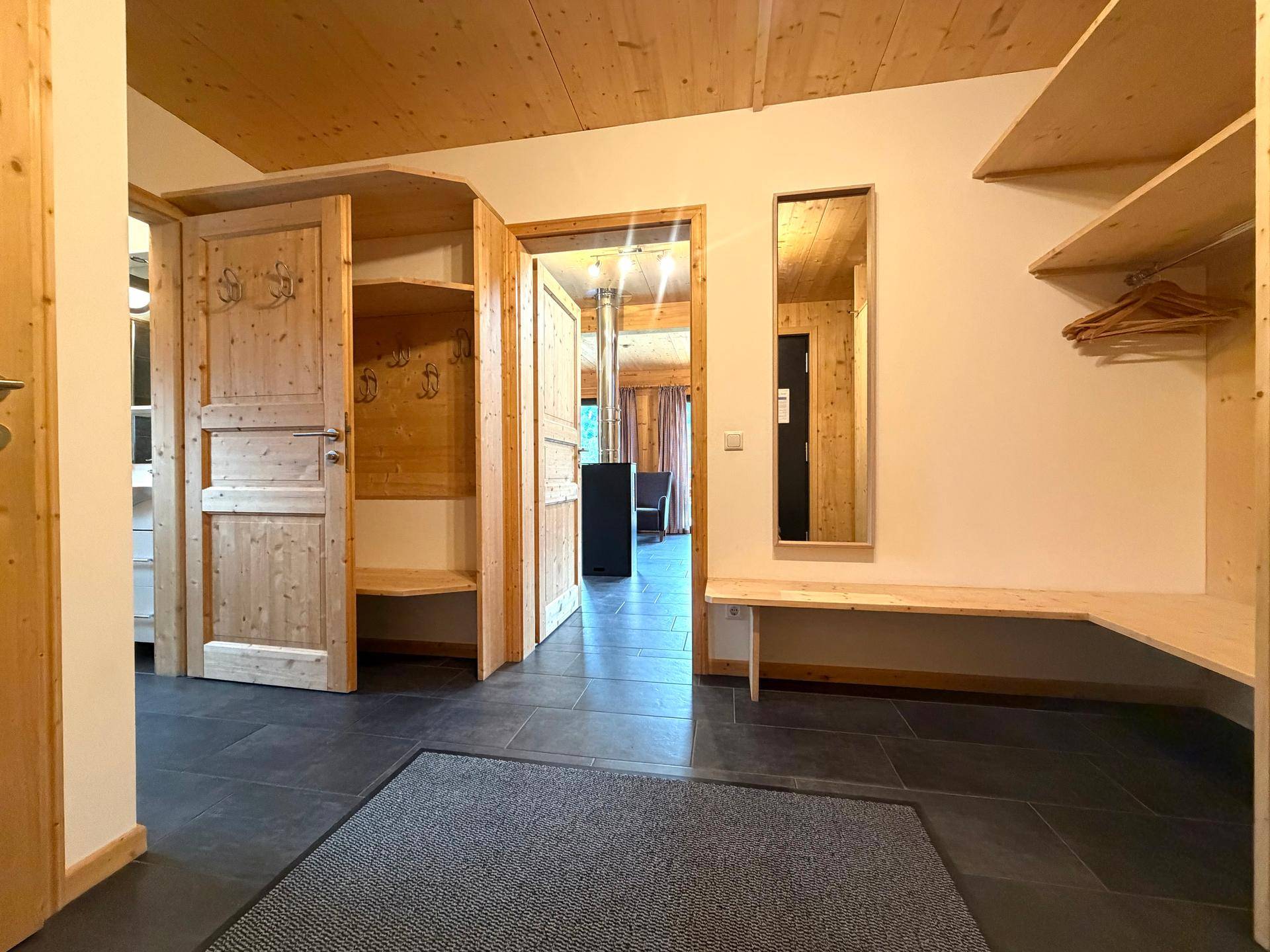 Eingangsbereich mit Holzbänken, Garderobe und Spiegel, führt zum Wohnbereich.