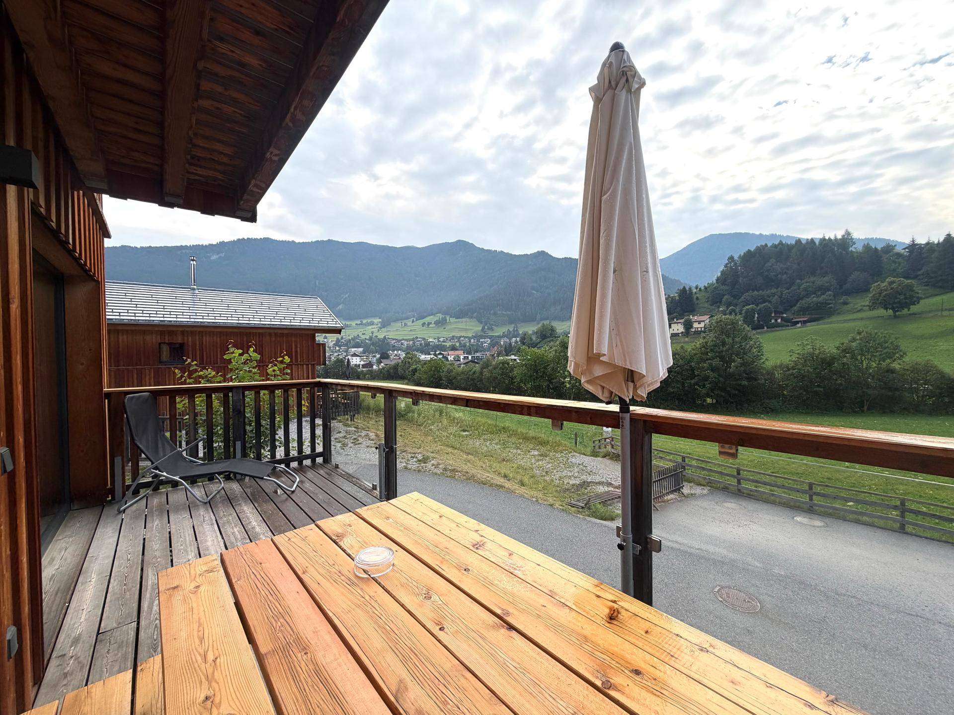 Balkon mit Holztisch und Sonnenschirm, bietet einen Panoramablick auf die umliegende Landschaft.