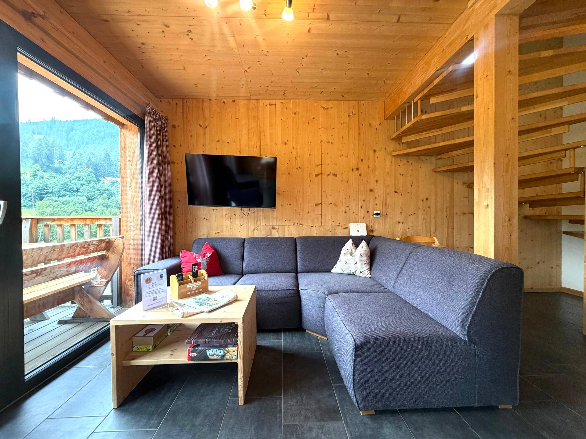 Gemütliches Wohnzimmer mit Ecksofa, Holzwänden und Zugang zu einem Balkon mit Aussicht.