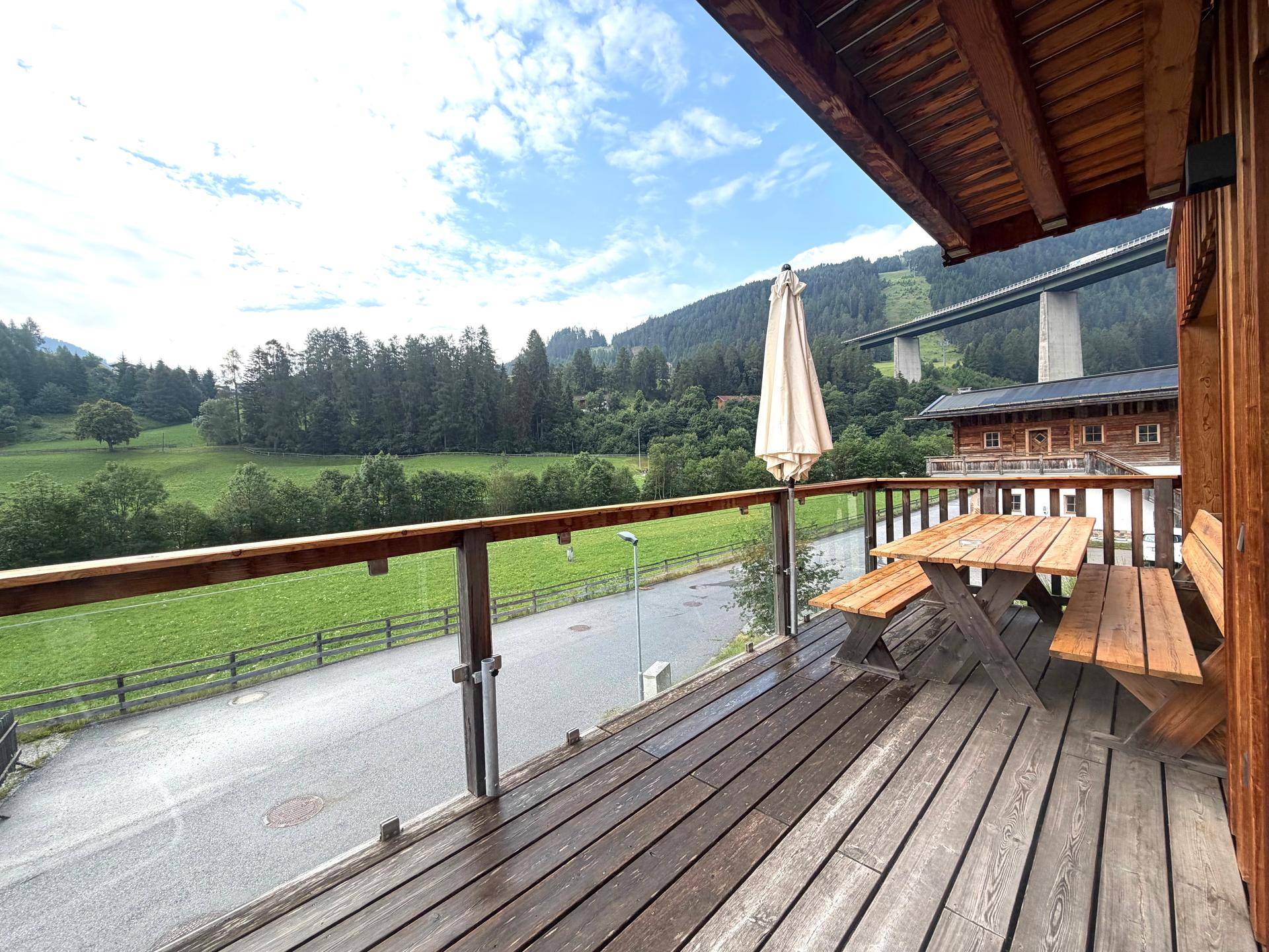 Geräumiger Holzbalkon mit Esstisch und Bänken, bietet weite Aussicht auf die Berge.