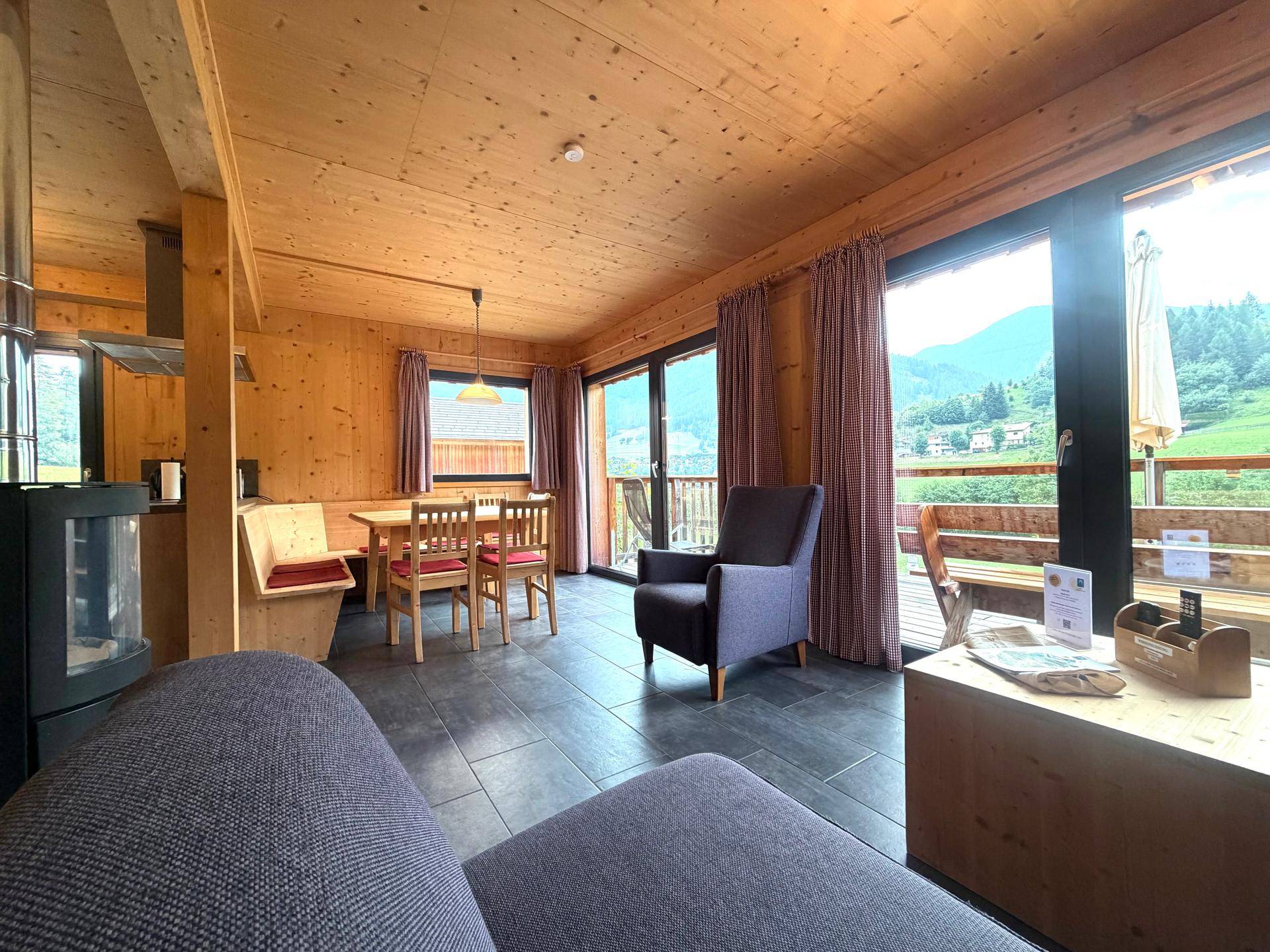 Heller Wohnbereich mit Holzwänden, großen Fenstern und Zugang zu einem Balkon mit Bergblick.
