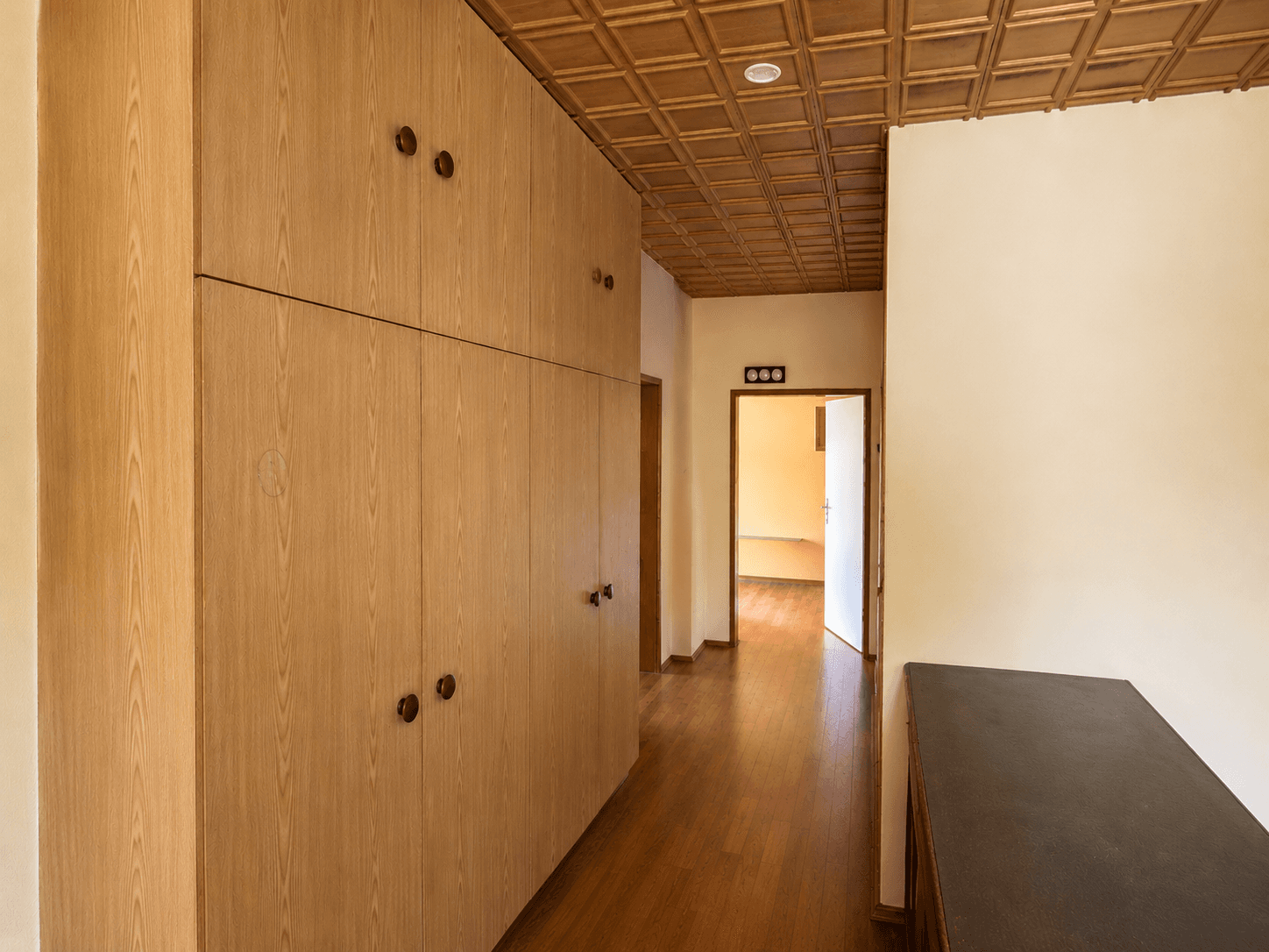 Langer Flur mit Holzboden, Einbauschränken und einer Holzdecke mit Kassettenmuster.